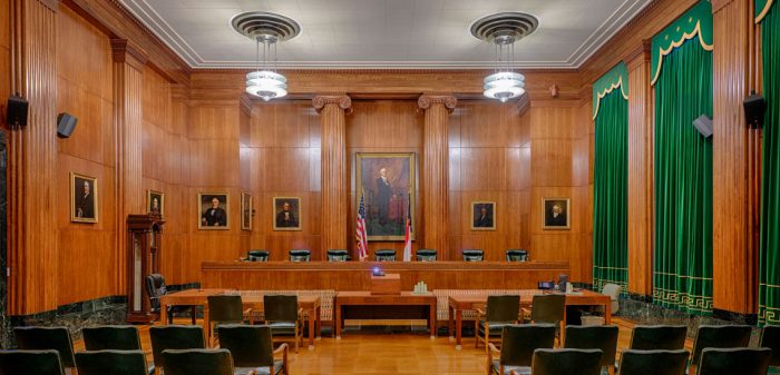 An empty court room with a panel for five judges, surrounded by tall, wood paneled walls and thick green velvet curtains.