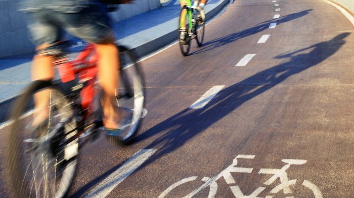 Two people bike rapidly through a marked bike lane on the street.