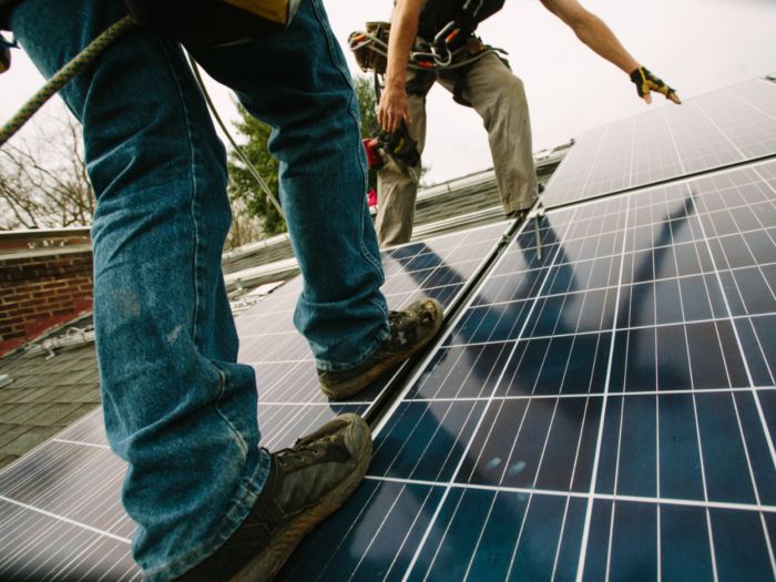 Two people are standing on a roof to install solar panels.