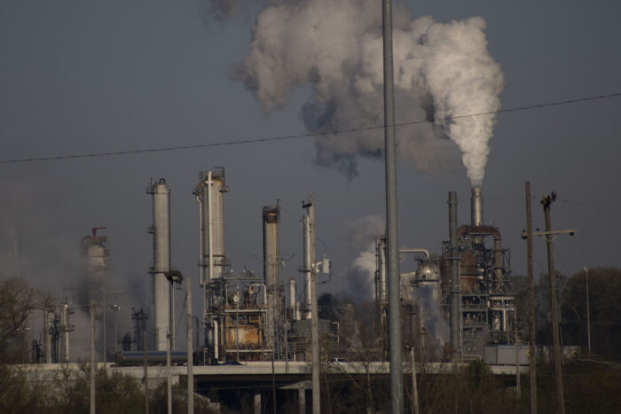 Gray and white clouds billow from a smokestack at an industrial facility.