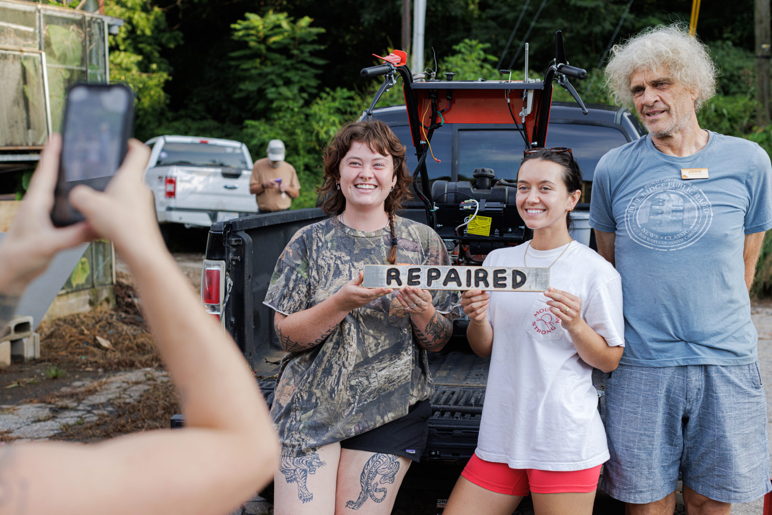 Two young women and an older man pose for a photo with a sign that reads 