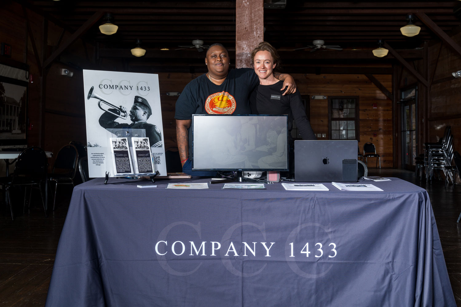Two women stand behind a table with materials celebrating Company 1433